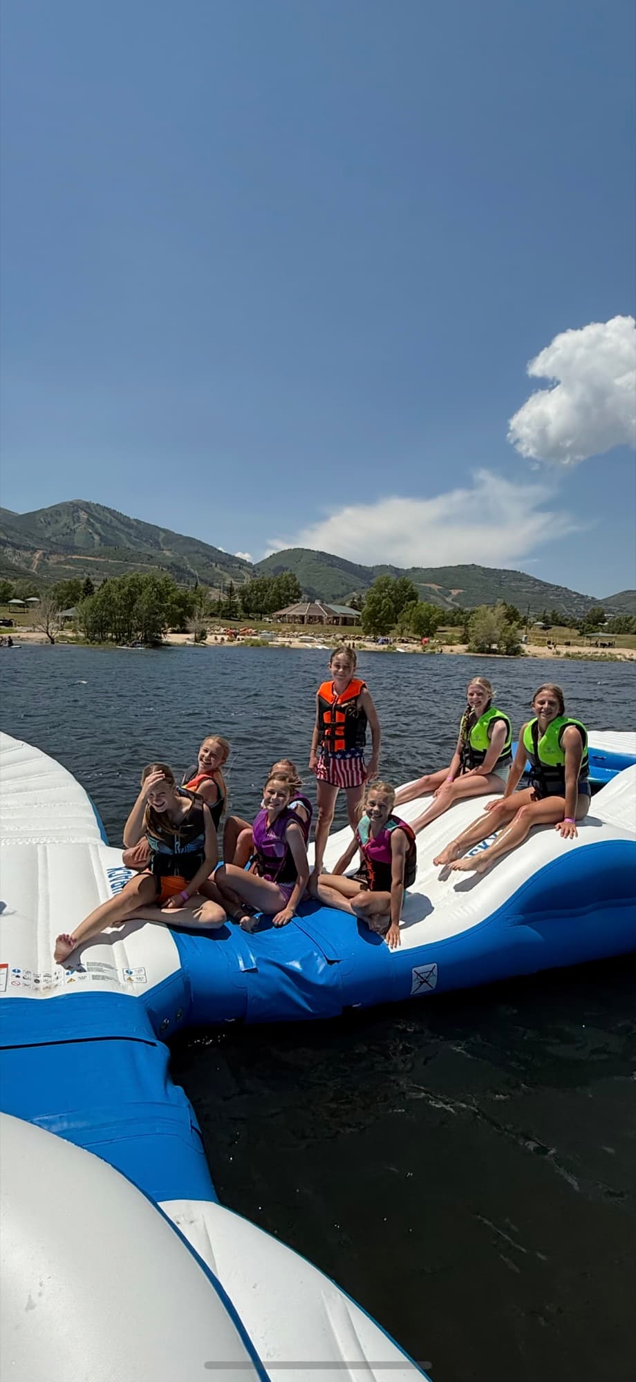 Guests on the Jordanelle Aqua Park, all wearing life jackets, with the Wasatch mountains behind