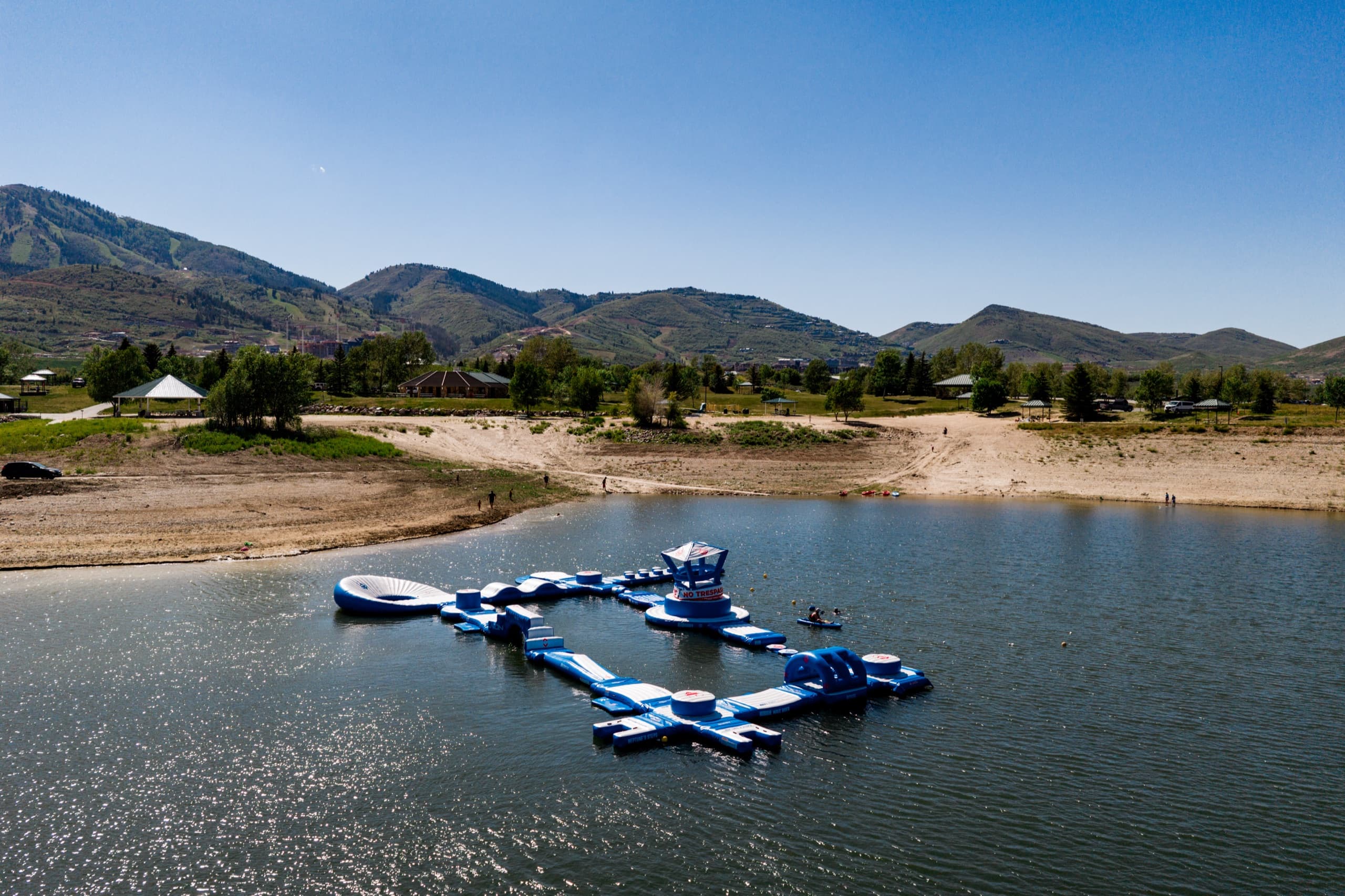 Aerial view of Jordanelle Aqua Park — a floating inflatable obstacle course on the reservoir with the Wasatch mountains behind