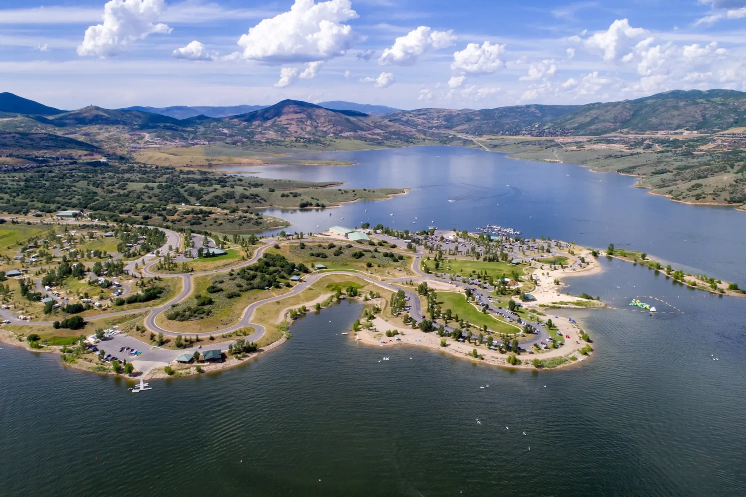 Aerial of Jordanelle marina and Hailstone Recreation Area — beach, boat slips, and parking just beyond the aqua park, with the Wasatch behind