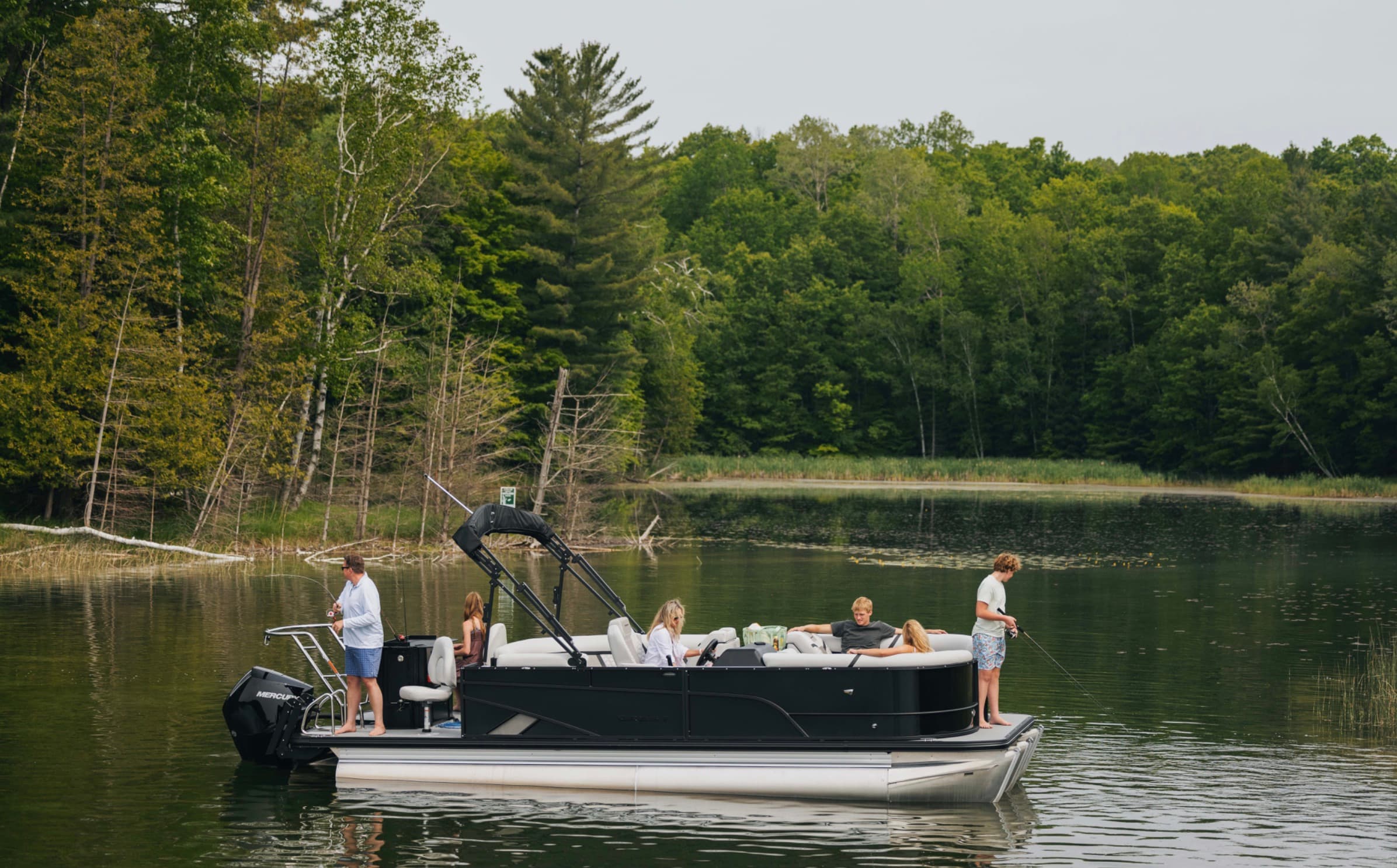 Black-hull pontoon boat with guests aboard, lines out fishing on a calm lake