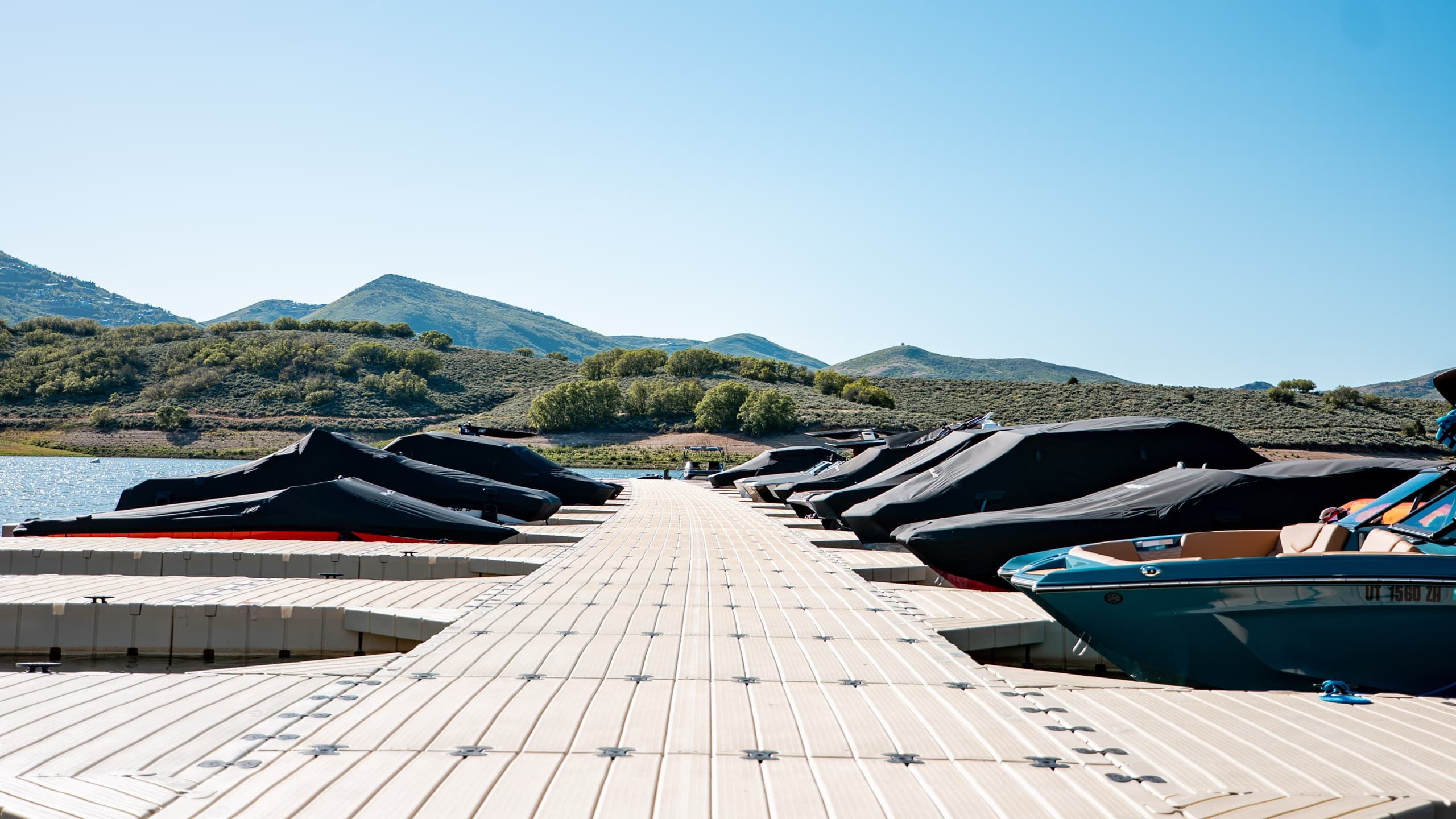 Covered boats lined up along the dock at Jordanelle Marina, ready for service and winterization, with the Wasatch foothills behind