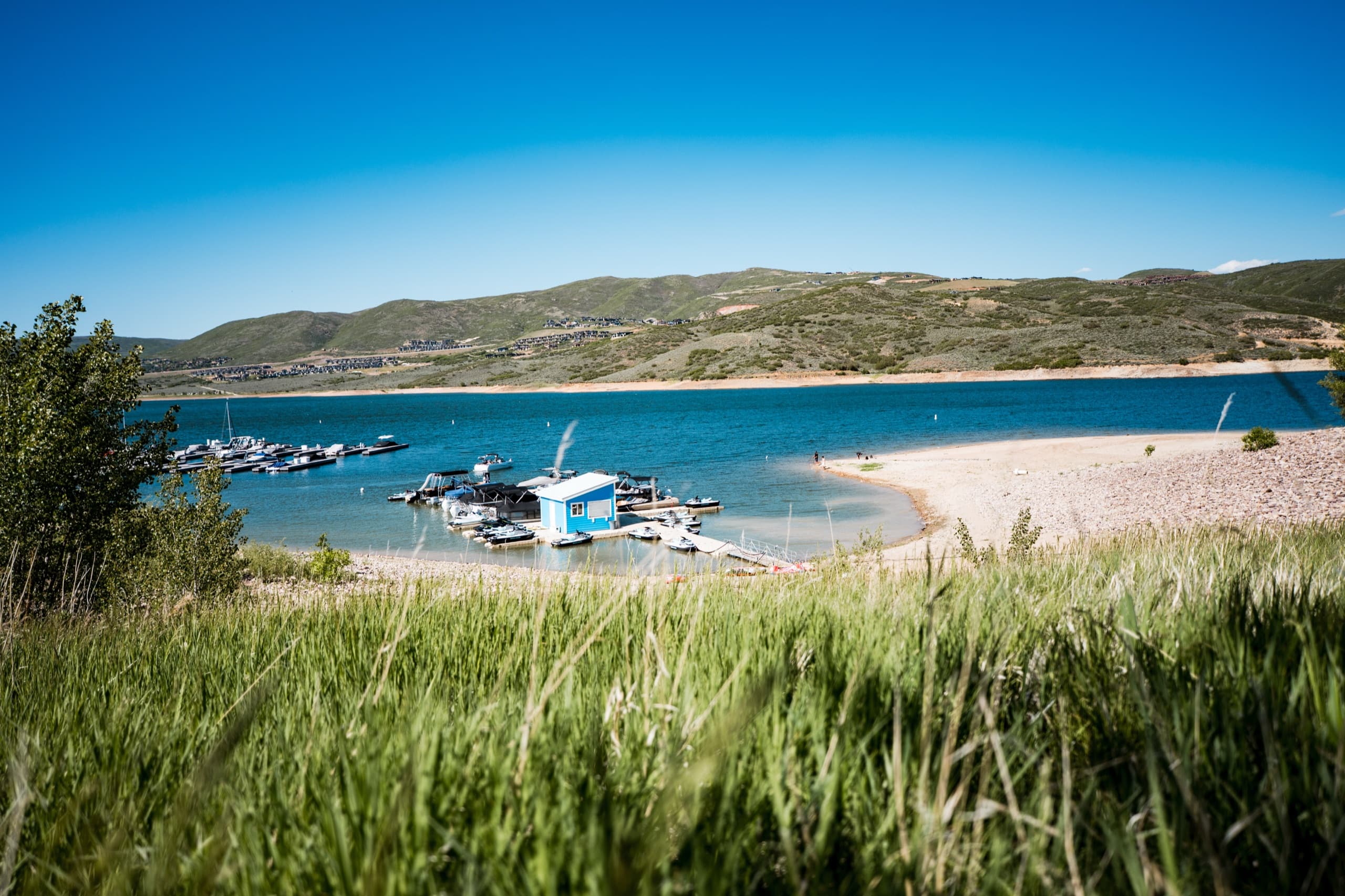 View of Jordanelle Marina from the beach — boathouse, docks, and boat slips with the Wasatch foothills behind