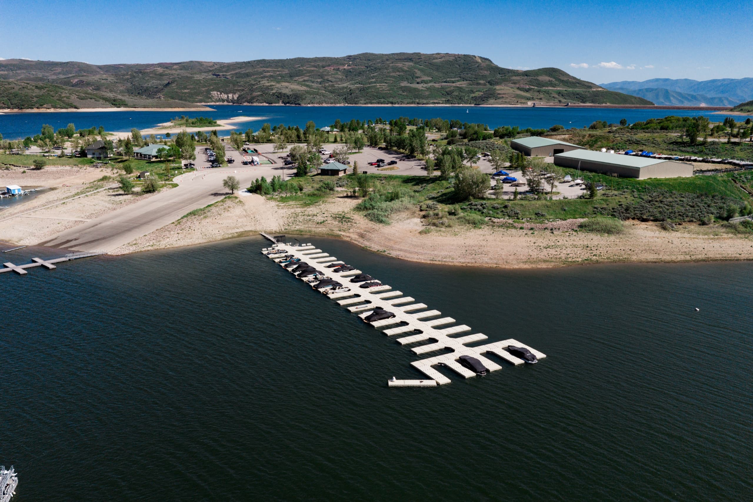 Aerial view of Jordanelle Rentals & Marina — boat slips, beach, launch ramp, and storage with the Wasatch mountains behind