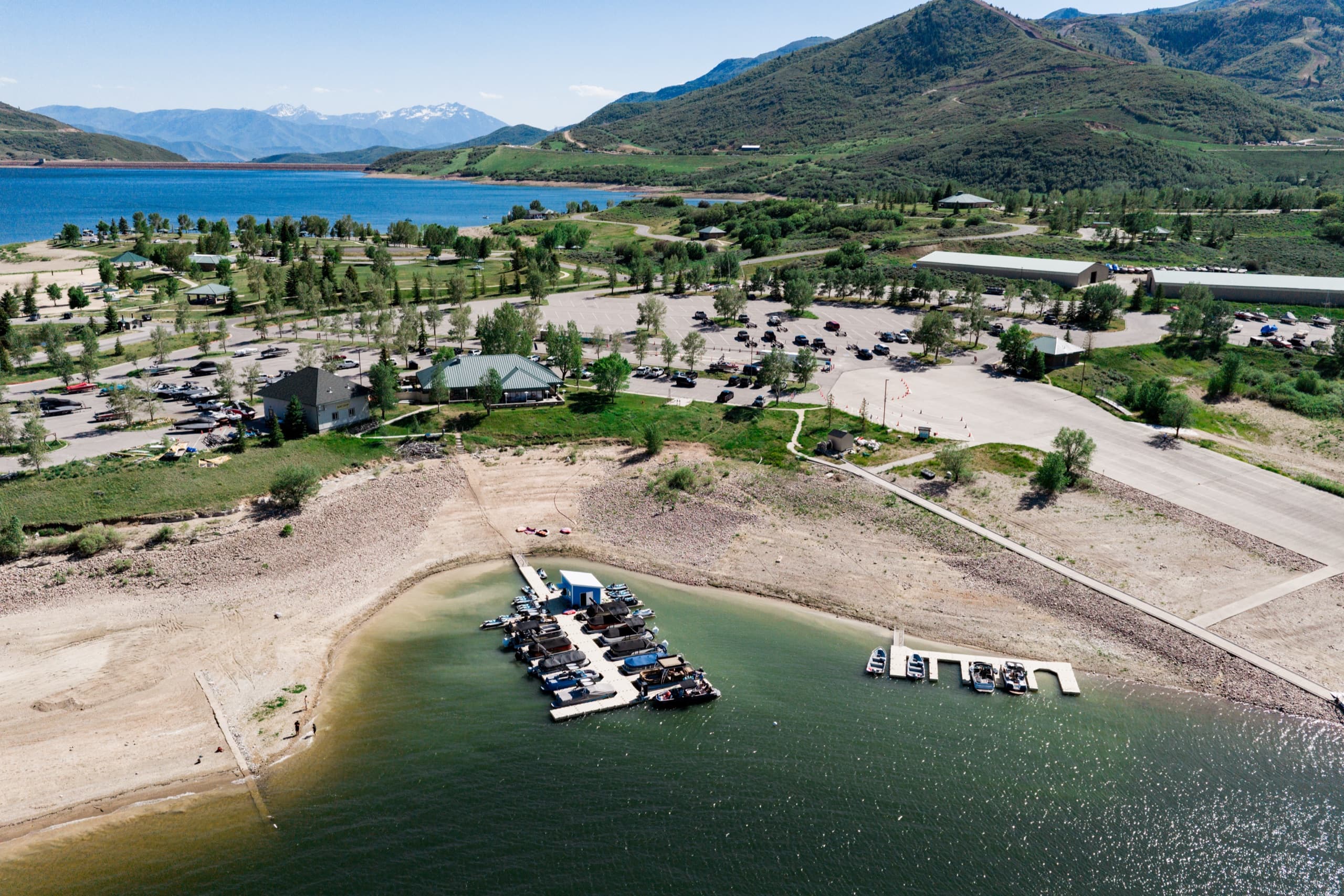 Wide aerial of Jordanelle Marina within the state park — boat slips, parking, and buildings along the reservoir with the Wasatch behind