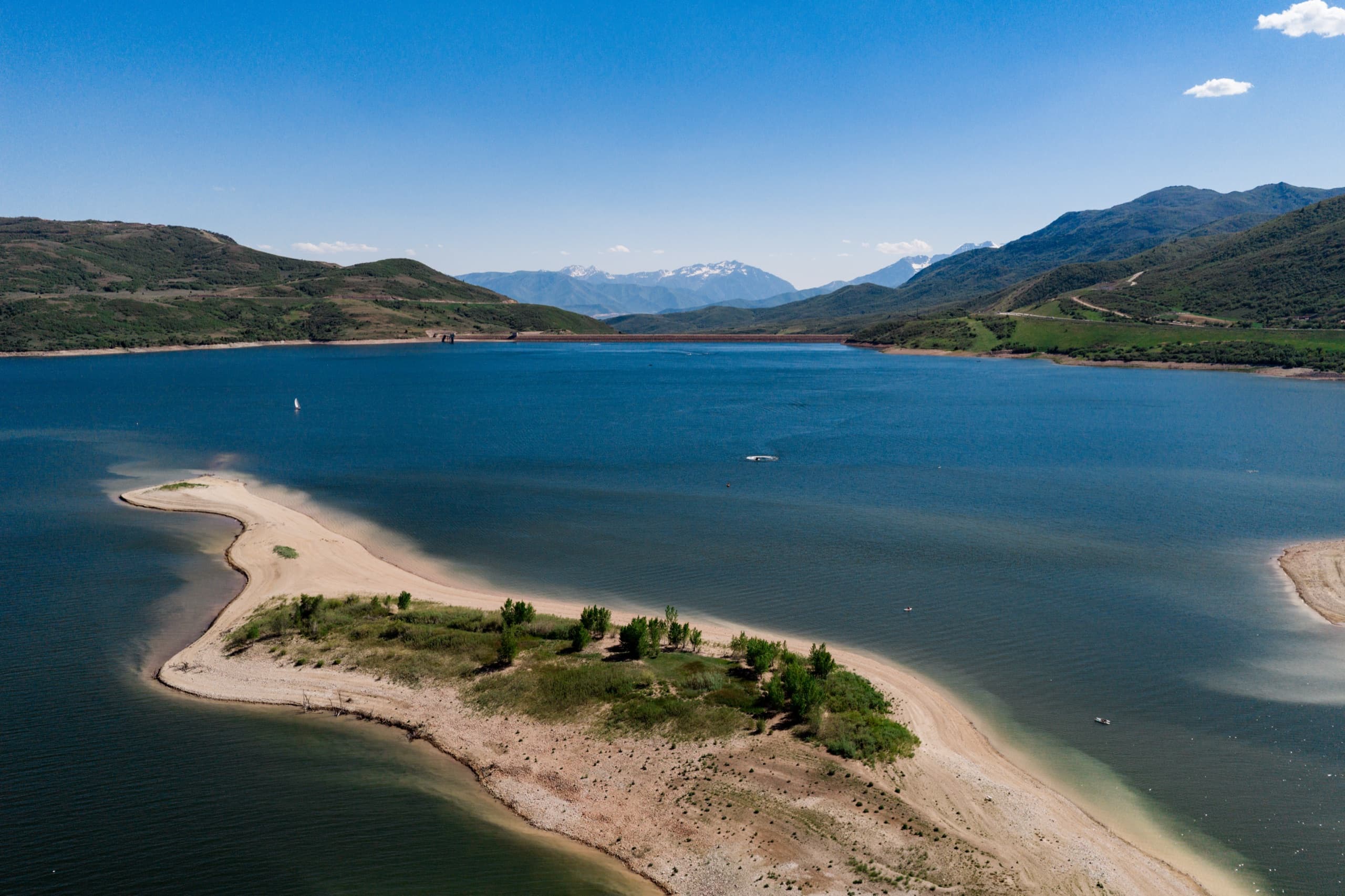 Aerial of a sandbar island in Jordanelle State Park with snow-capped peaks beyond
